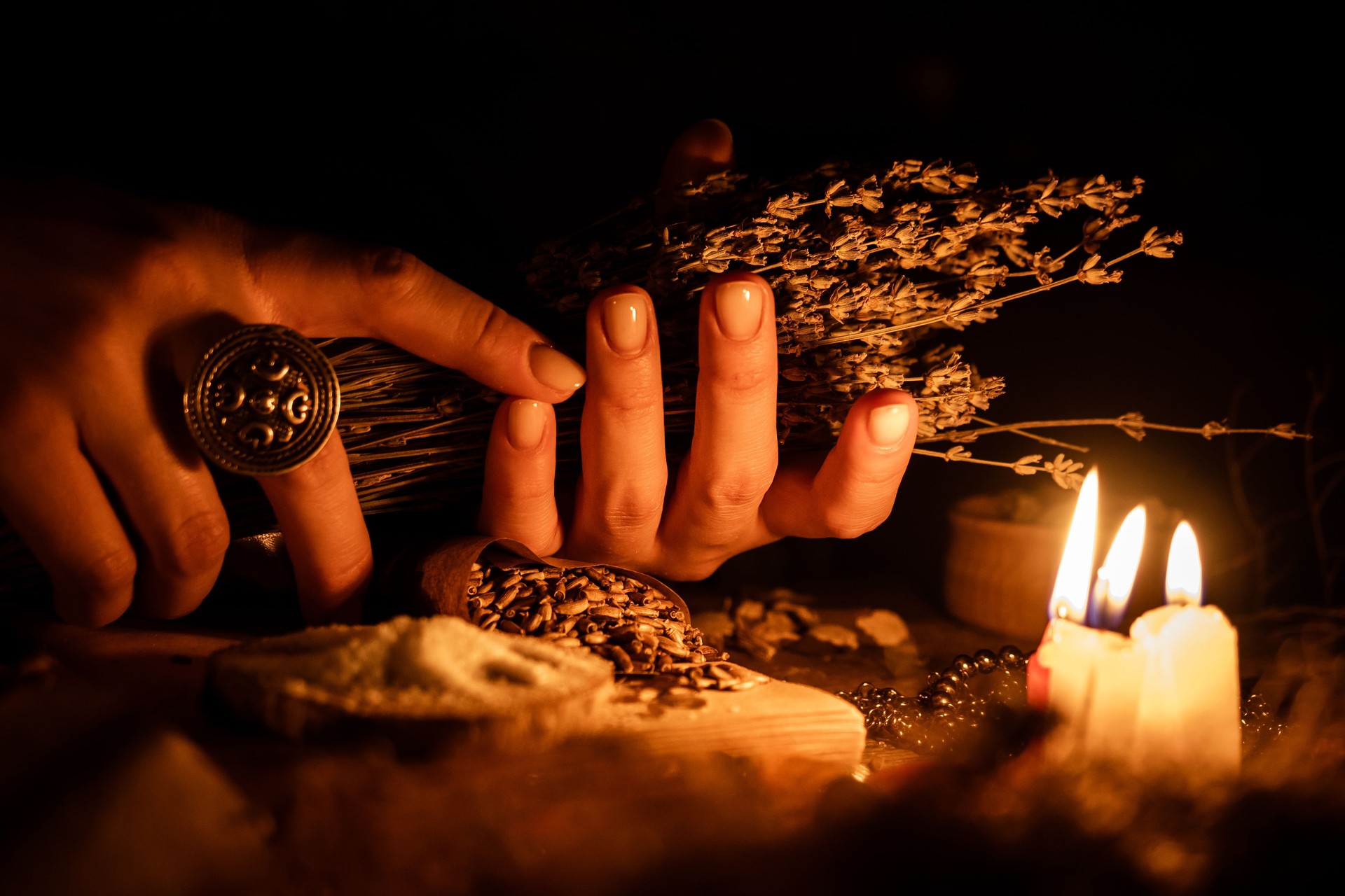 In the hands of the witches bunch of dry herbs for divination. The light from the candles on the old magic table. Attributes of occultism and magic