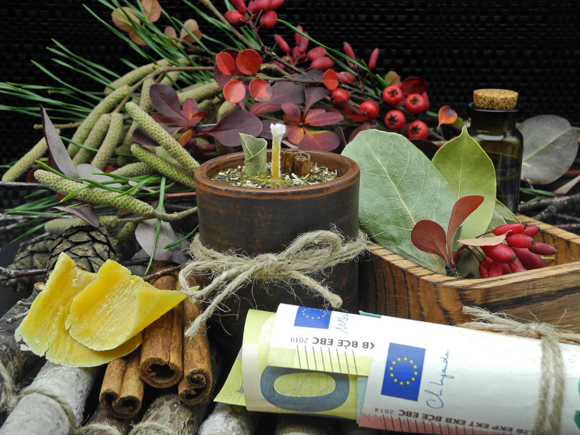 Herbal ritual candle to attract money in clay pot between natural ingredients on black background